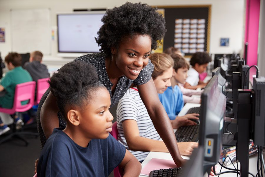 A teacher looking over a student's shoulder as they both look into a computer monitor in a classroom